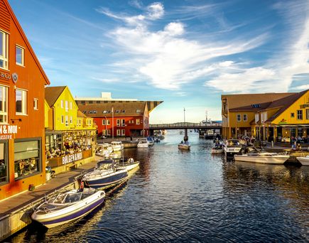 Farbenfrohe Architektur am Wasser mit Booten, die an einem hellen, sonnigen Tag entlang eines belebten Hafens anlegen. Warme Atmosphäre mit Menschen, die die malerische Aussicht und die lebendige Umgebung der charmanten Gegend genießen
