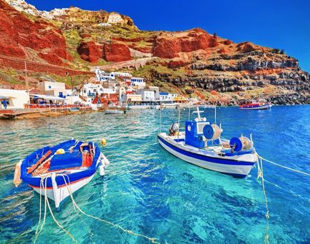 Die ikonischen weißen Gebäude von Santorini, Griechenland, die sich an die Klippen schmiegen und das tiefblaue Ägäische Meer überblicken, mit einem Kreuzfahrtschiff im Hintergrund.