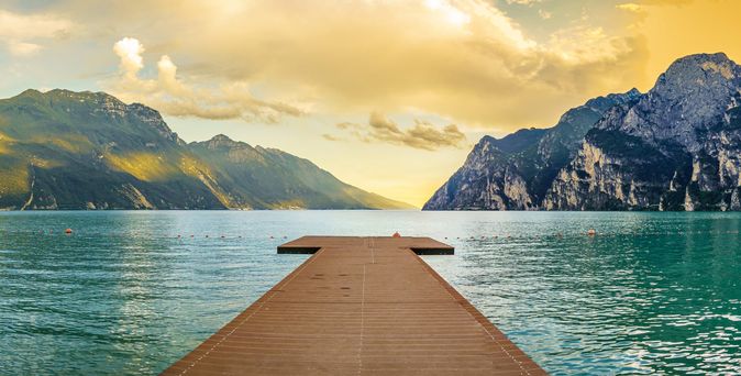 Eine Holzbrücke, die in einen See oder Fluss führt, mit Bergen im Hintergrund.