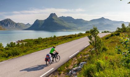 Ein Fahrradfahrer fährt entlang eines Sees mit Blick auf Berge und die Stadt bei Sonnenuntergang.