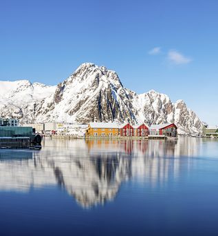 Eine norwegische Küstenstadt mit bunten Häusern am Wasser, umgeben von schneebedeckten Bergen.