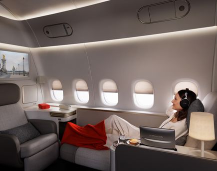 La Première Cabin im Flugzeug, Frau mit Kopfhörern und roter Decke