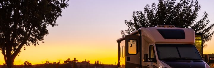 Ein Campervan steht am Ufer eines Sees oder Flusses bei einem malerischen Sonnenuntergang.