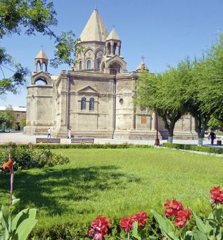 Gebäude Zipfelturm in Armenien im Vordergrund grüne Wiese und rote Blumen