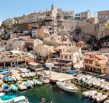 Eine malerische Küstenstadt mit vielen Booten, die im Hafen liegen. Die Häuser sind in warmen Farben gehalten und schmiegen sich an den Hang, während sich das Meer bis zum Horizont erstreckt.