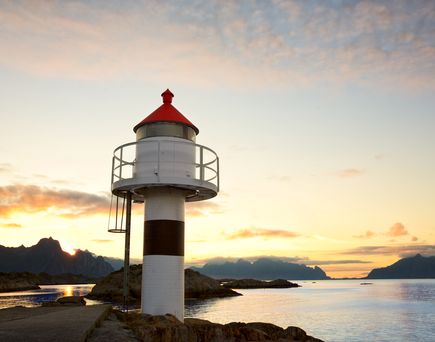 Ein rot-weißer Leuchtturm steht auf einer felsigen Küste bei Sonnenuntergang.