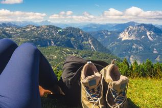 Ein Paar Wanderschuhe und ein Wanderrucksack stehen auf einem Felsen, mit einem malerischen Bergsee und hohen Gipfeln im Hintergrund.