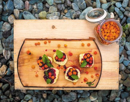 Einige Beeren und Snacks auf einem Holzbrett, welches auf Kieselsteinen steht.