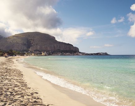 Ein Sandstrand mit türkisfarbenem Wasser, umgeben von Bergen.