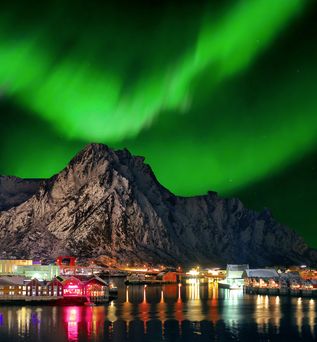 Die Nordlichter in leuchtendem Grün über einer norwegischen Küstenstadt in der Nacht.