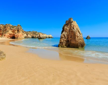 Strand an der Algarve. Blick über den Sand auf einen Felsen der aus dem Wasser ragt