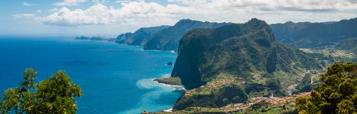 Eine Küstenlandschaft mit Klippen, die ins blaue Meer abfallen, und einer Stadt am Ufer.
