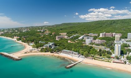Eine Luftaufnahme eines Strandes mit goldenem Sand, türkisfarbenem Wasser und Hotels.