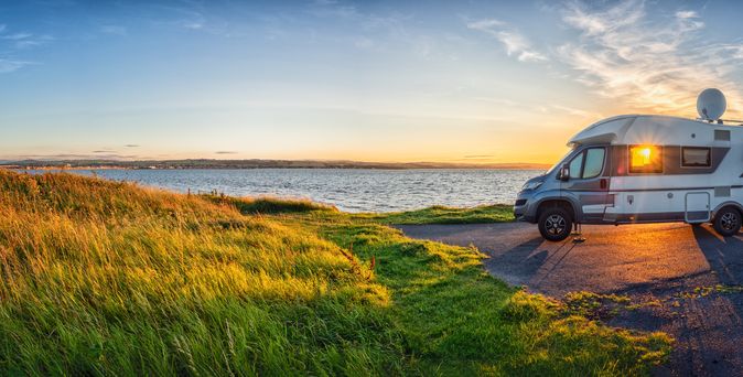 Ein Wohnmobil steht idyllisch in der schottischen Wildnis, umgeben von grünen Hügeln und Bergen, unter einem bewölkten Himmel, was auf "Wild Camping" hindeutet.