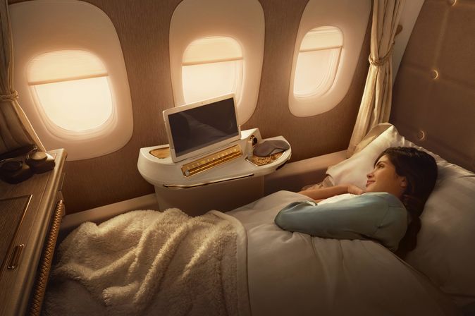 Reisende schläft zugedeckt in einem vollständig ausgestatteten Bett mit Entertainment-System in der Emirates First Class Suite.