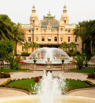 Ein prunkvolles historisches Gebäude mit einem Brunnen und einem gepflegten Garten. Die Architektur ist symmetrisch und beeindruckend.