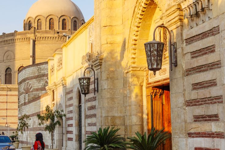 Die historische Hängende Kirche (Church of St. George) in Kairo, mit ihrer markanten Architektur und einem runden Kuppelbau im Hintergrund, bei hellem Tageslicht.