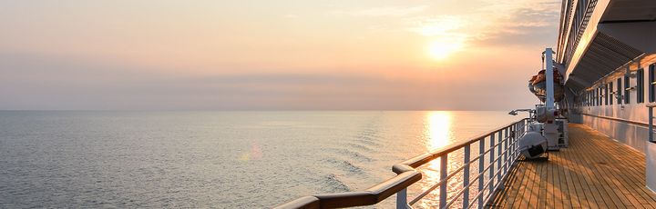 Sonnenuntergang auf dem Meer, aufgenommen vom Außendeck eines Kreuzfahrtschiffes mit hölzernem Boden und Geländer.