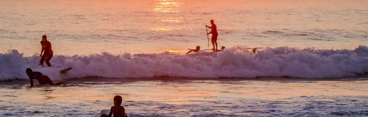 Eine Person surft bei Sonnenuntergang am Strand, mit Blick auf das Meer.