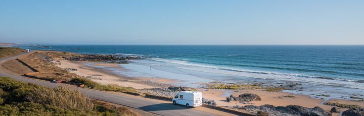 Camper fährt entlang einer Küstenstraße am Meer mit felsigem Strand 