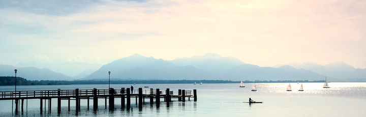 Ein langer Holzsteg führt in einen ruhigen See, umgeben von grüner Landschaft bei Sonnenuntergang.