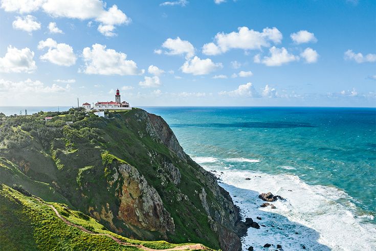 Steilküste in Portugal. Auf der Klippe steht ein Leuchtturm. Am fuß schäumt das Meer
