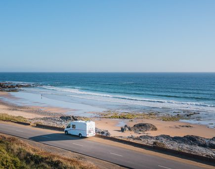 Eine Reihe von Wohnwagen und Wohnmobilen sind auf einem Campingplatz, Costa do Vizir Camping, nahe der Küste geparkt, umgeben von Bäumen und grünen Flächen.