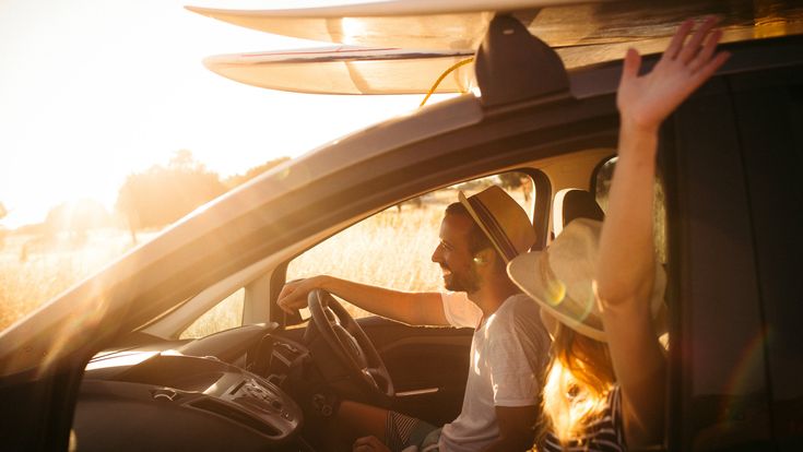 Eine Person fährt Auto, mit Surfbrettern auf dem Dach, bei Sonnenuntergang.