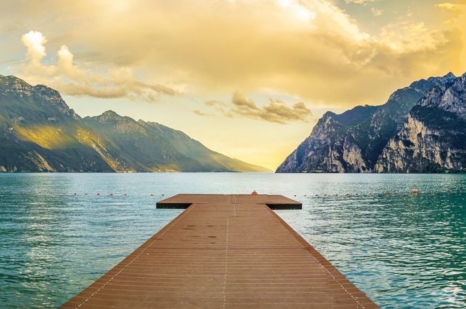 Eine Holzbrücke, die in einen See oder Fluss führt, mit Bergen im Hintergrund.