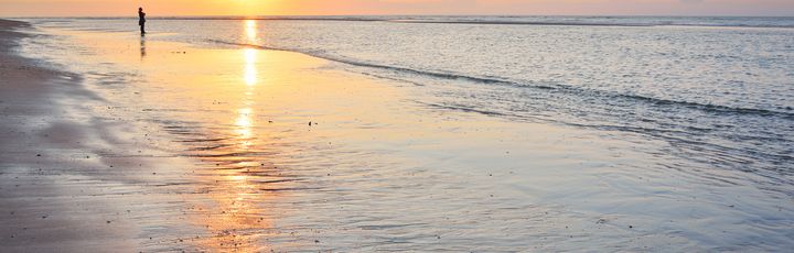 Sonnenuntergang am Strand. Ein Mann spaziert den Flutsaum lang.