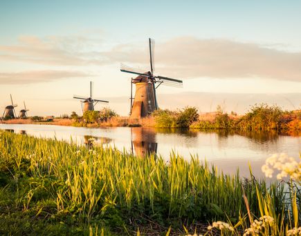 Eine Windmühle in einer Landschaft mit einem Fluss und Feldern.