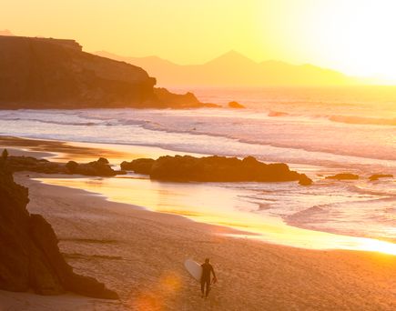 Eine Landschaft mit einem Strand und Bergen bei Sonnenuntergang.