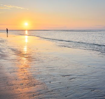 Sonnenuntergang am Strand. Ein Mann spaziert den Flutsaum lang.