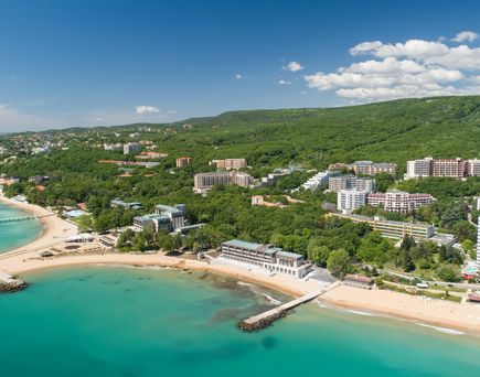 Eine Luftaufnahme eines Strandes mit goldenem Sand, türkisfarbenem Wasser und Hotels.