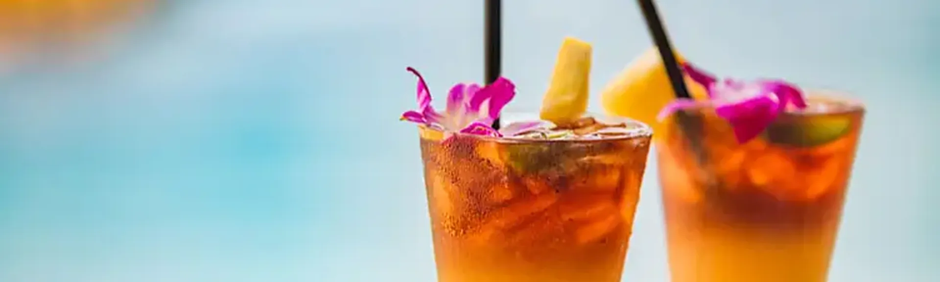 zwei fruchtige Cocktails mit Strohhalm stehen am Poolrand. Im Hintergrund ist das Wasser zu sehen