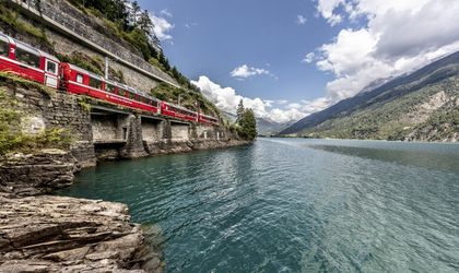 Zug fährt durch eine bergige Landschaft mit grüner Natur neben einem Fluss