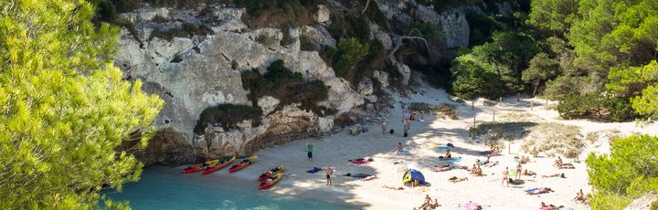 Eine Bucht mit Sandstrand und türkisblauem Wasser, umgeben von grüner Vegetation.