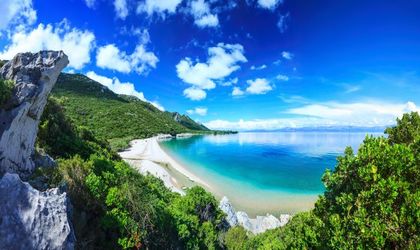 Eine Küstenlandschaft mit einem Strand, Bergen und türkisfarbenem Wasser.