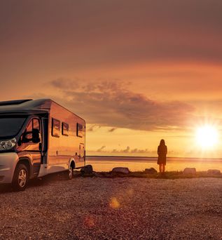 Ein Campervan steht am Ufer eines Sees oder Flusses bei einem malerischen Sonnenuntergang.