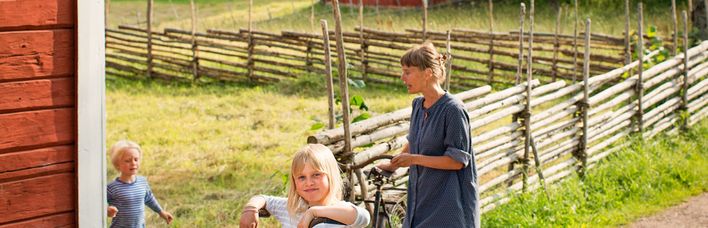 Ein traditionelles schwedisches Holzhaus mit einem roten Dach und einem Fahrrad davor. Die Szene ist ländlich und idyllisch.