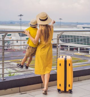 Frau und Kind in gelb mit gelbem Koffer am Flughafen