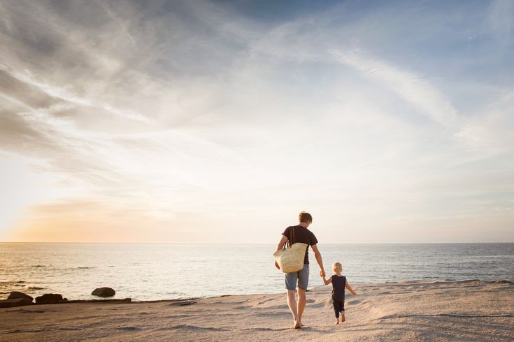 Eine einzelne Person geht am Strand entlang, während die untergehende Sonne den Himmel in warme Orangetöne taucht und sich im ruhigen Meer spiegelt.