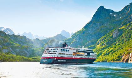 Hurtigruten Kreuzfahrtschiff auf einem Fjord im Hintergrund grüne Berge 