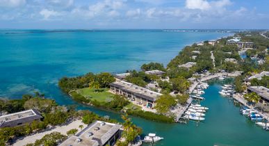 Blick auf Buttonwood Bay auf Key Largo. Einige Häuser auf kleinen Inselchen, davor kleine Boote, Meer und Palmen. Blauer Himmel.