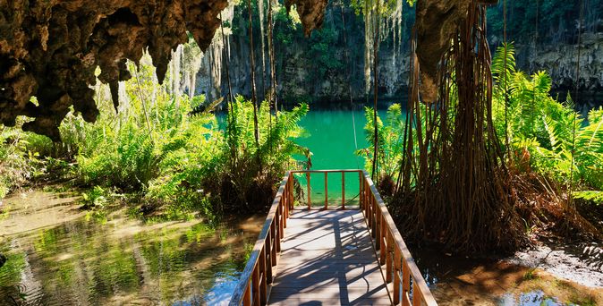 Tres Ojos Santo Domingo: Holzsteg führt durch eine üppig bewachsene Tropfsteinhöhle zu einem smaragdgrünen Naturpool inmitten des Dschungels.