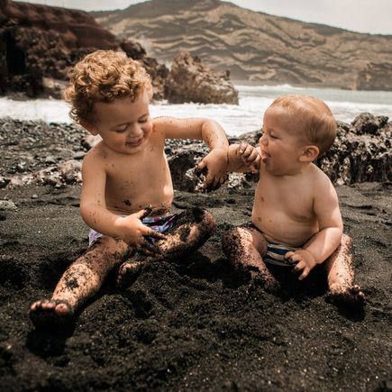 Kinder spielen im schwarzen Sand