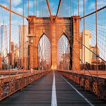 Die Brooklyn Bridge in New York City am frühen Morgen, mit ihren ikonischen gotischen Bögen und Stahlseilen, die sich über den East River spannen, im Hintergrund die Skyline von Manhattan.