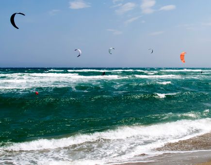 Ein Surfer gleitet auf einer Welle am Strand, während die Sonne auf das Meer scheint. Die Wellen sind kräftig und das Wasser türkisfarben.
