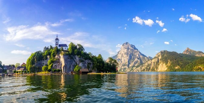Der Traunsee mit dem Schloss Ort im Vordergrund, umgeben von Bergen.