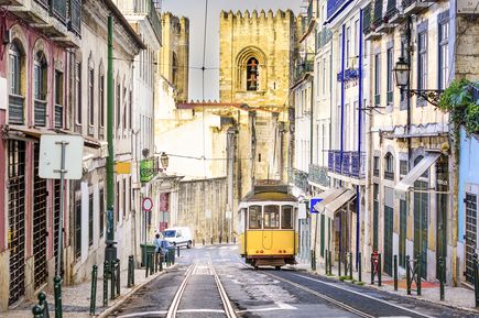 Eine gelbe Straßenbahn fährt eine Straße in Lissabon, Portugal, hinunter.